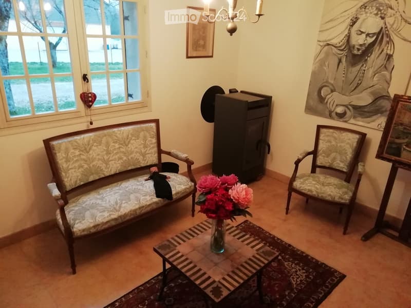Living room with a patterned sofa, armchair, coffee table with a vase of flowers, and a chandelier hanging from the ceiling.