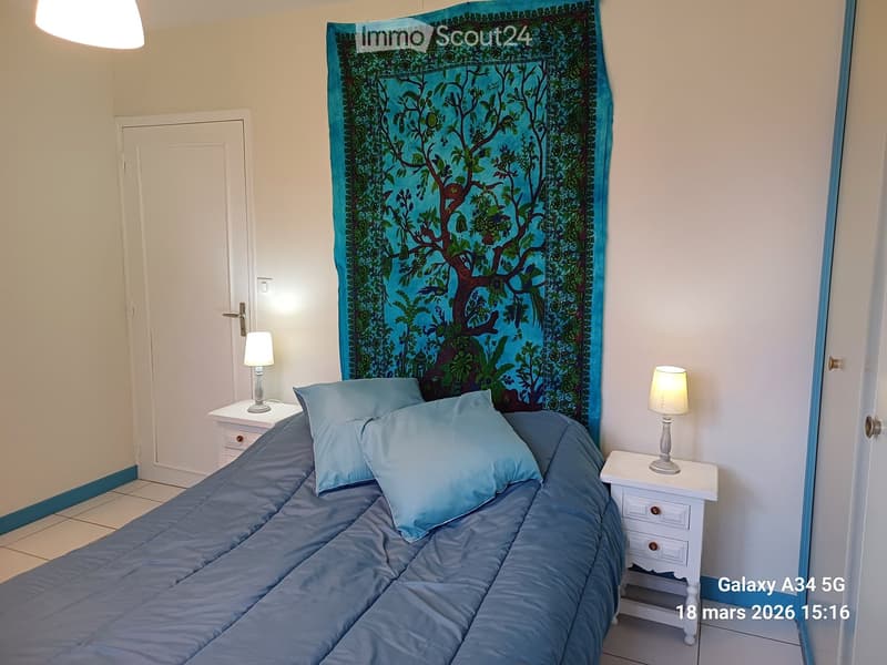 Bedroom with a neatly made bed, two nightstands with lamps, and a colorful tapestry on the wall.