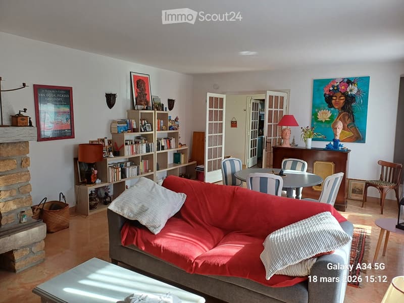 Living room with a red sofa, coffee table, bookshelf, dining table, chairs, lamps, and artwork.