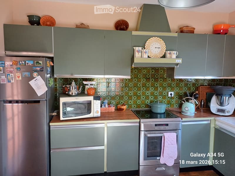 A modern kitchen with grey cabinets, stainless steel appliances, and a patterned backsplash. The counter features a microwave, teapot, and other kitchen items.