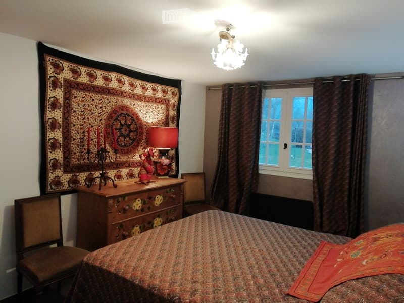 Cozy bedroom with a patterned bedspread, wooden nightstand, table lamp, decorative tapestry, and a chandelier.