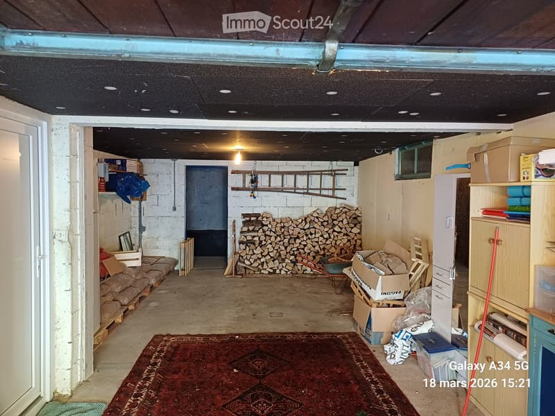 Empty storage room with concrete floor, exposed brick walls, and scattered storage items including boxes, shelves, and a pile of firewood.