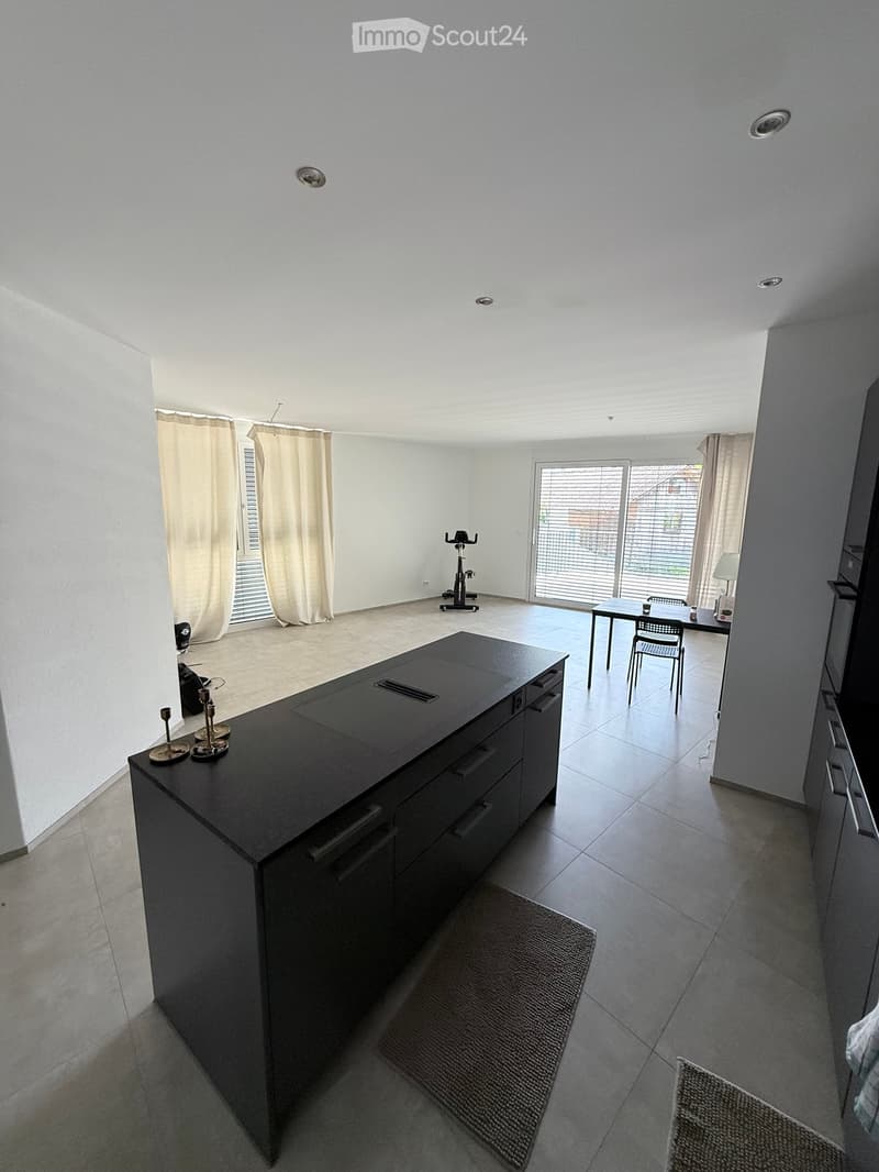 Modern kitchen with a black island, dining table, exercise bike, and large windows with curtains.