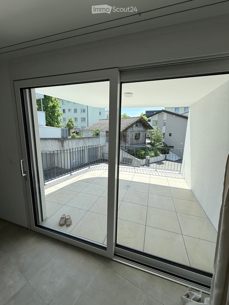 Balcony with tiled floor, metal railing, and a pair of shoes placed on the floor.