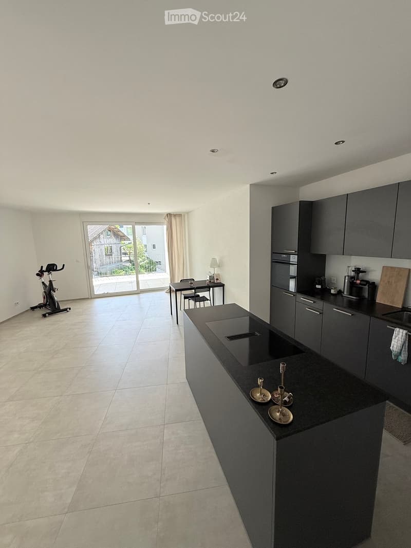 Modern kitchen with dark grey cabinets, black island, exercise bike, small dining table, and various appliances.
