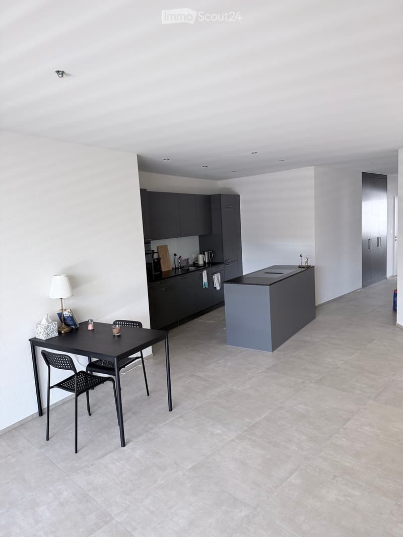 Modern kitchen with dark grey cabinets, a central island, a dining table with chairs, and various kitchen appliances.