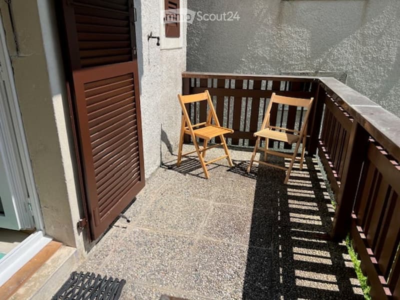 Balcony with two wooden folding chairs, wooden railing, and a view of the building exterior.