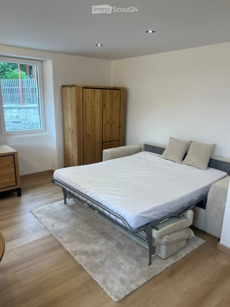 Bright bedroom with wooden flooring, a double bed with white bedding, a wooden wardrobe, a nightstand, and a soft rug.