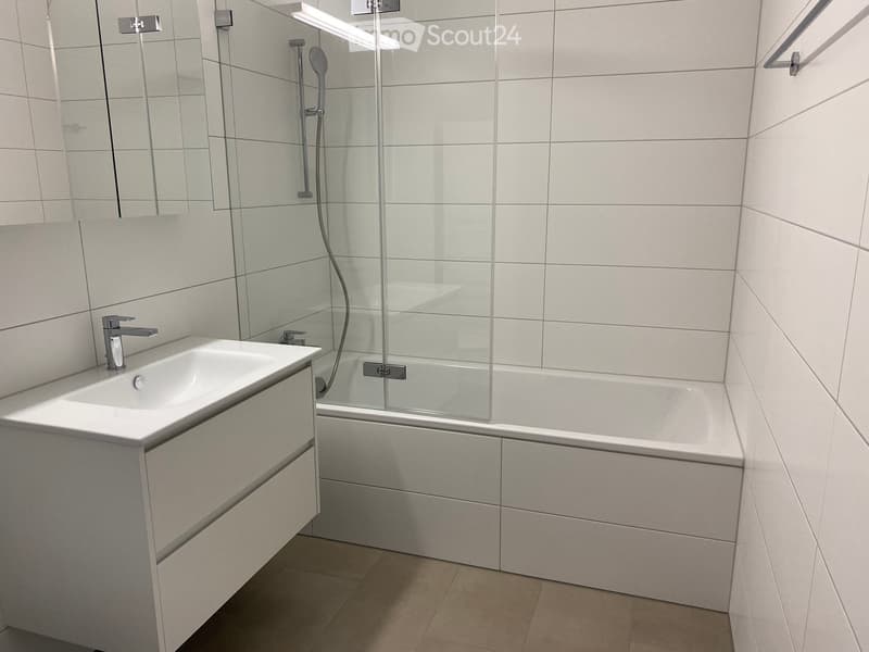 modern bathroom with white tiles, white bathtub, white sink, white cabinet, glass shower enclosure, shower head, mirror
