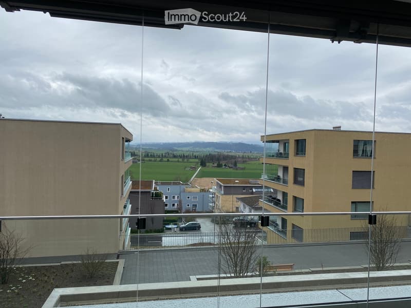 View from a window of a building with a parking lot, cars, and a field in the distance