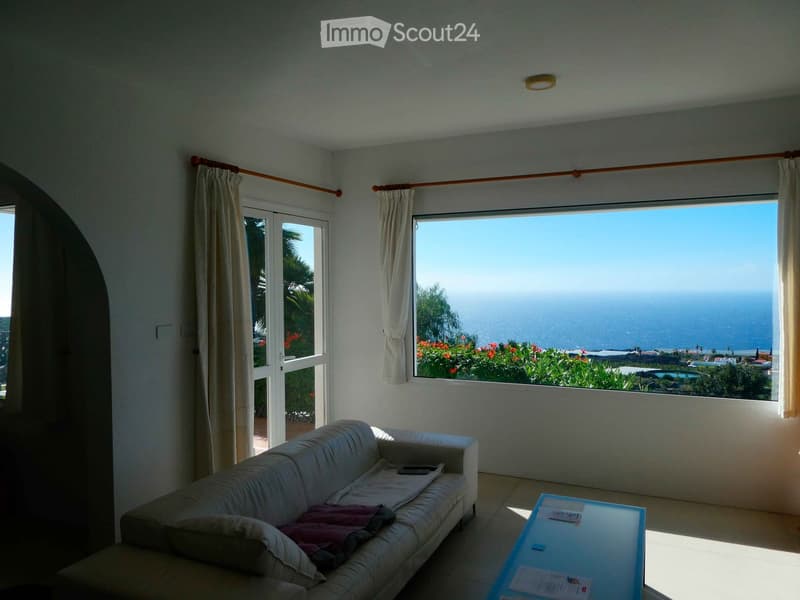 Bright living room with large windows offering a scenic ocean view, featuring a white sofa and a glass coffee table.