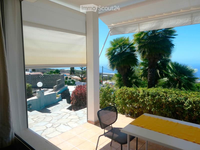Balcony with a table, chair, and a view of palm trees and the sea.