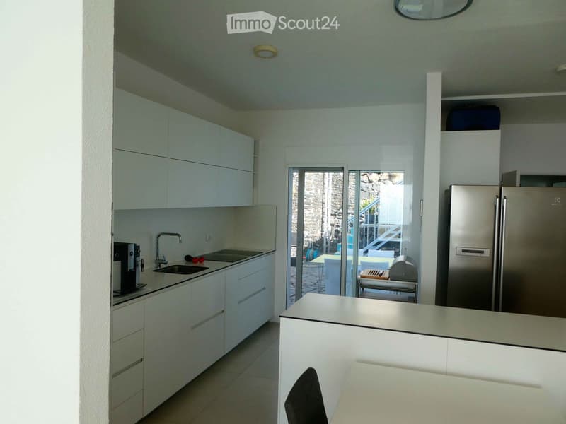 Modern kitchen with white cabinets, stainless steel appliances, and a large island counter. Features a sink, faucet, coffee machine, and a refrigerator.