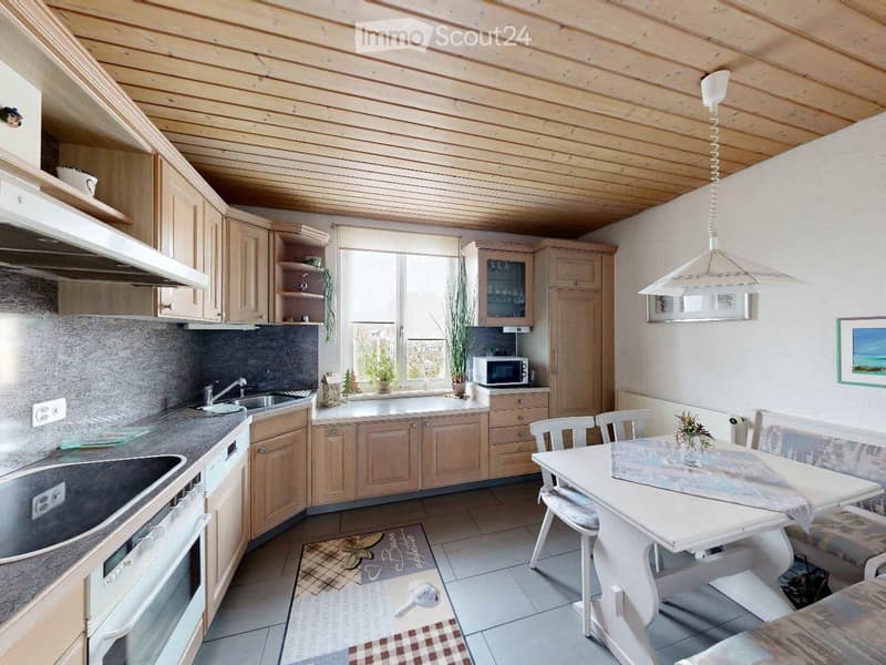 Bright kitchen with wooden cabinets, stainless steel appliances, a white dining table with chairs, and a pendant light fixture.