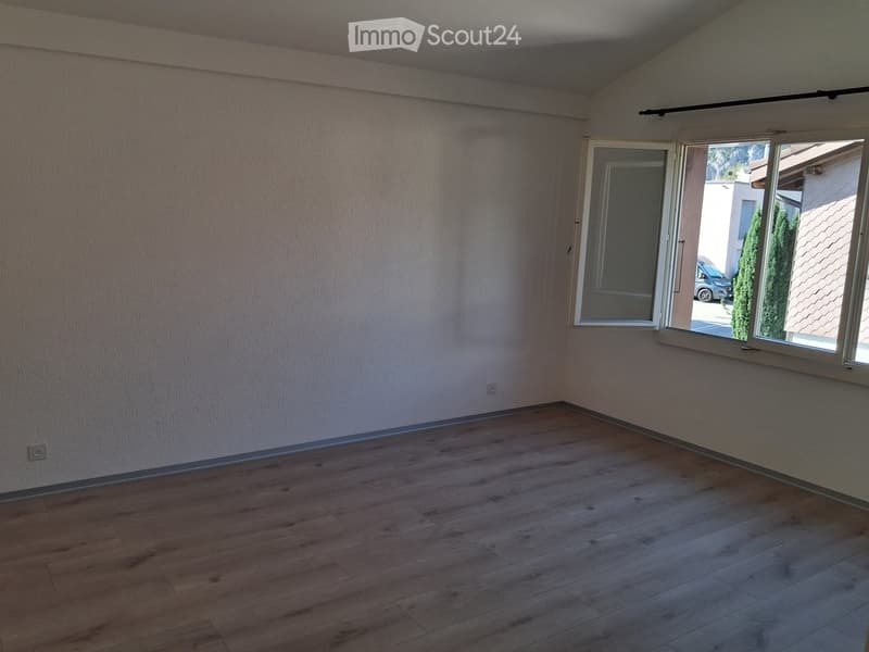 Empty room with wooden flooring and white walls, featuring large windows and a sliding door leading outside.