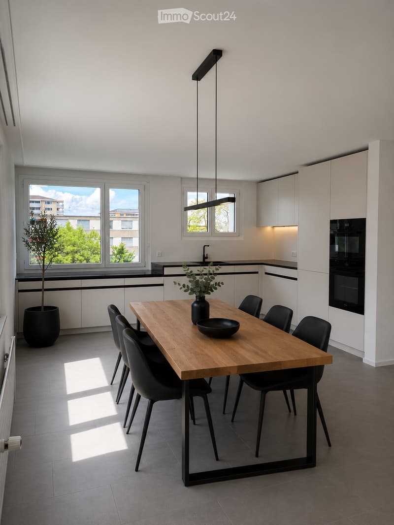 Modern kitchen with white cabinets, a wooden dining table, black chairs, a vase with greenery, and a bowl on the table. Large windows provide natural light, and a potted plant is placed near the window.