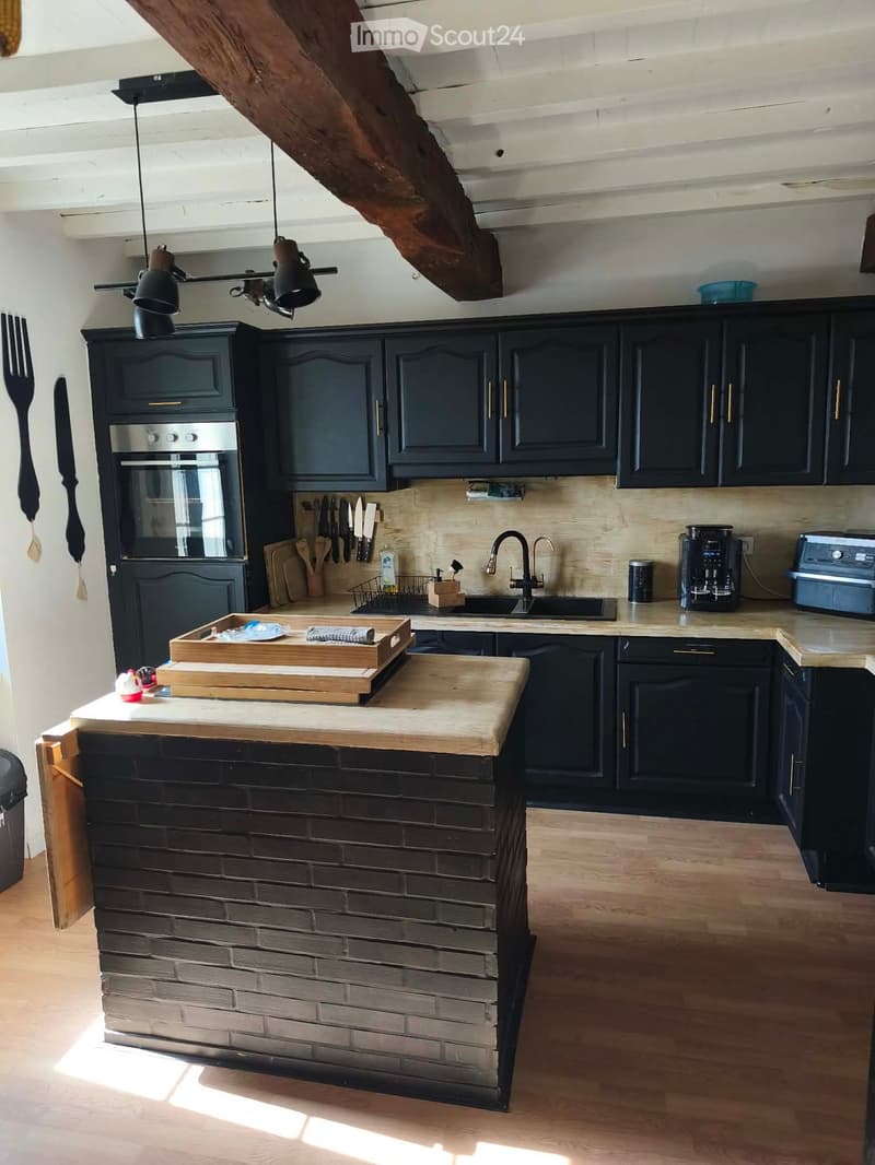 Modern kitchen with dark cabinets, wooden island, stainless steel appliances, and exposed wooden beams.