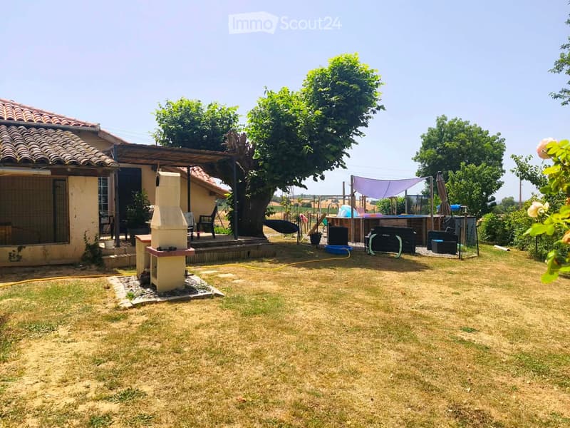 Lawn area with a house, outdoor furniture, barbecue, and trees.