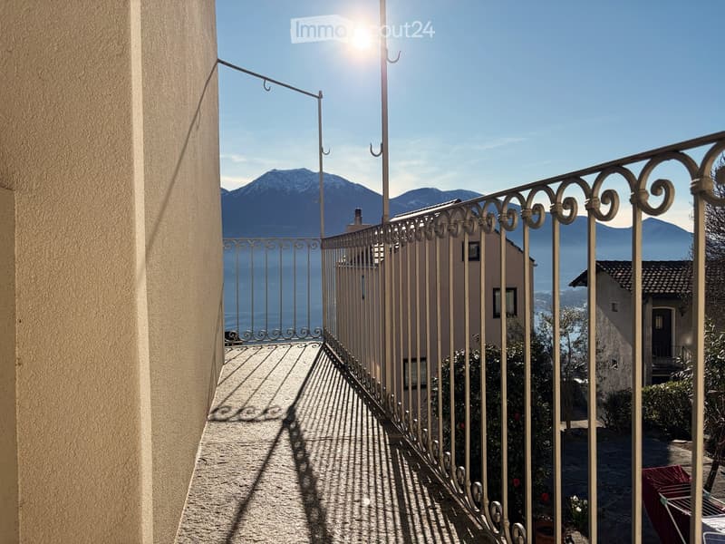 Balcony with metal railings, lake view, mountain view, shadows on the floor, sun shining