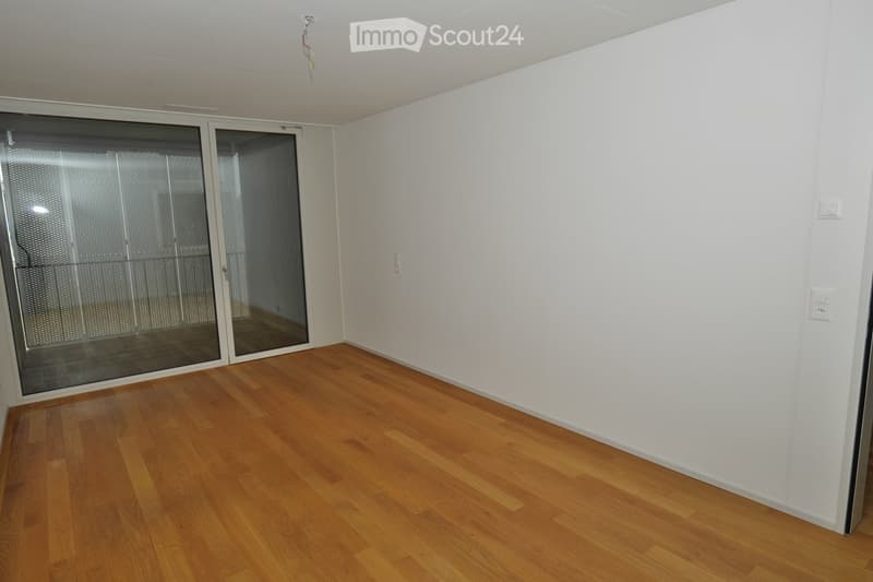 Empty room with wooden flooring, white walls, and large sliding glass doors leading to another space.