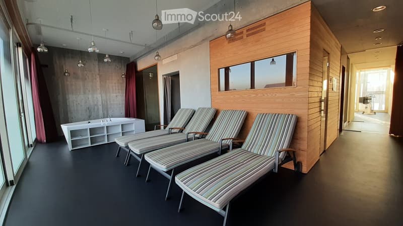 Modern, minimalist room with three sun loungers, a white storage unit, and a large mirror. The space features exposed concrete walls, wooden paneling, and pendant lights.