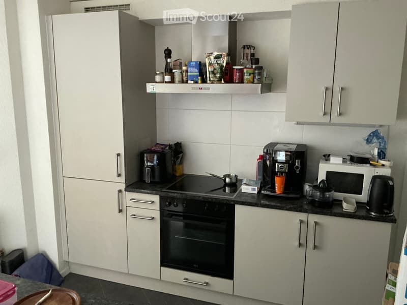 Modern kitchen with white cabinets, black countertop, and various appliances including an oven, coffee maker, microwave, kettle, and induction stove.