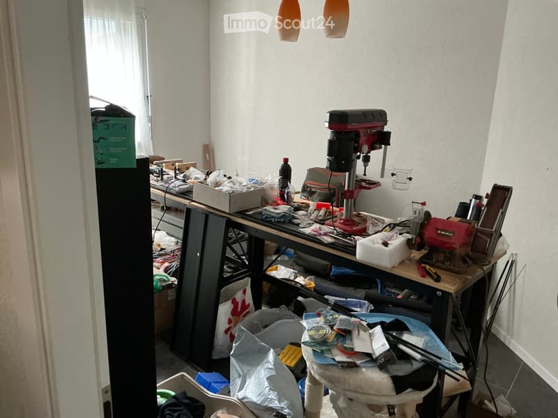 A cluttered workshop or utility room with a workbench, tools, a cat tree, and various items scattered around.