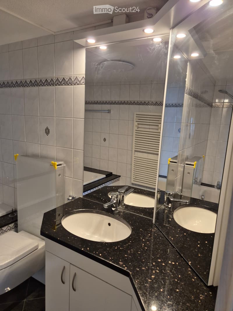 Modern bathroom with black granite countertop, two sinks, chrome faucets, large mirror, radiator, and toilet.