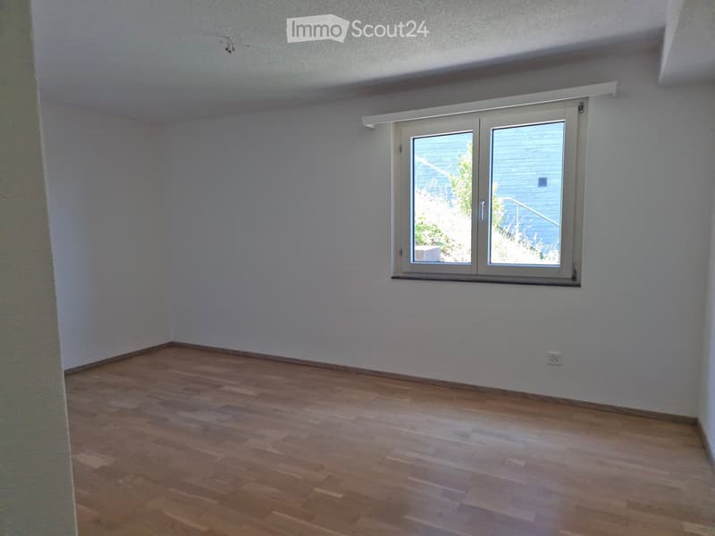 Empty room with wooden flooring and white walls, featuring a large window with a view of the outside.