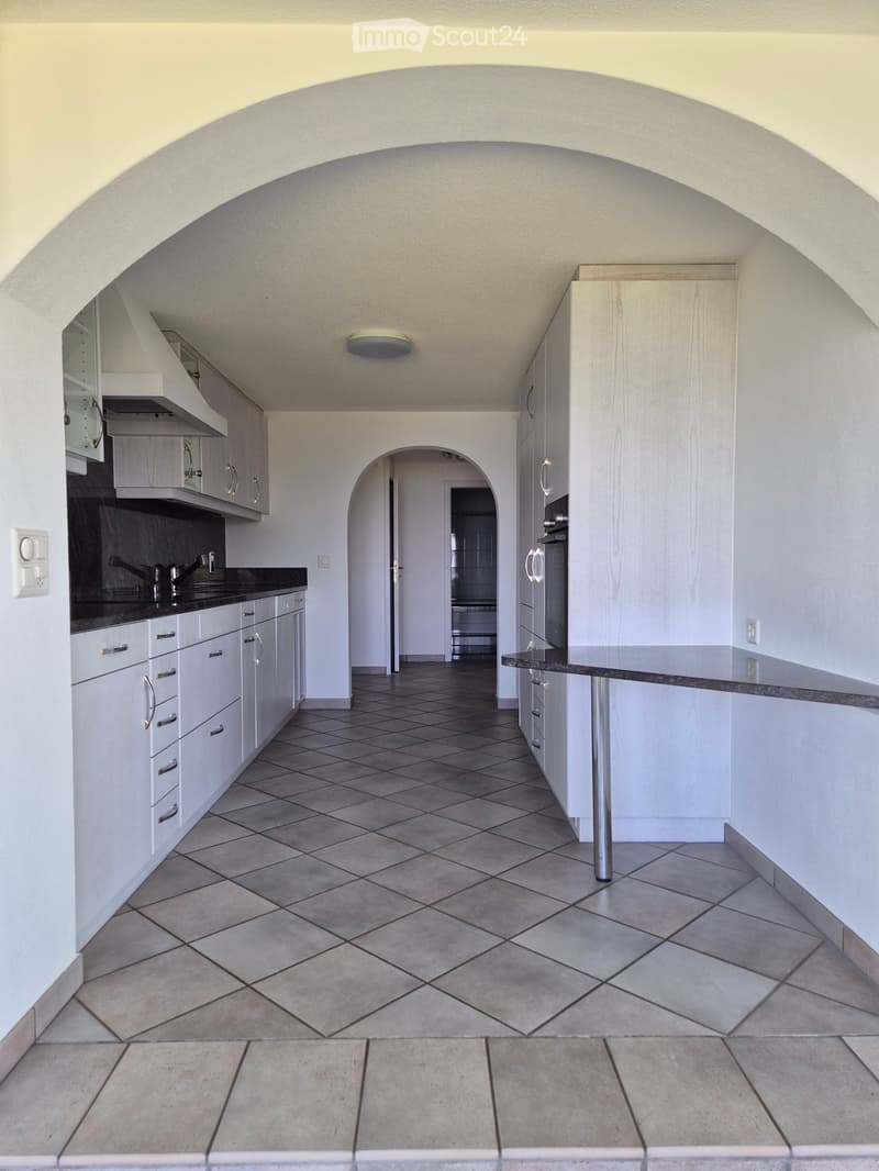 Modern kitchen with white cabinets, dark countertops, and tiled flooring. Features a sink, oven, and a central island with a countertop.