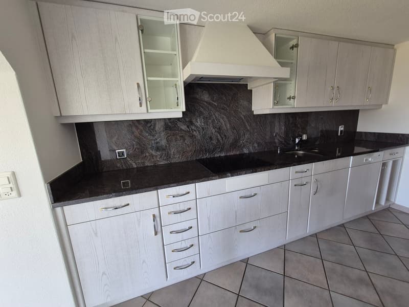 Modern kitchen with light wood cabinets, black countertop, stainless steel sink, and range hood.