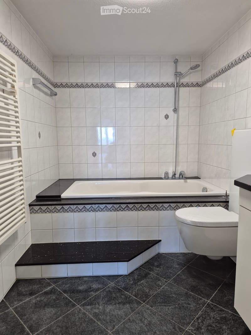 Modern bathroom with white tiles, a bathtub, toilet, shower, and a radiator on the left wall.