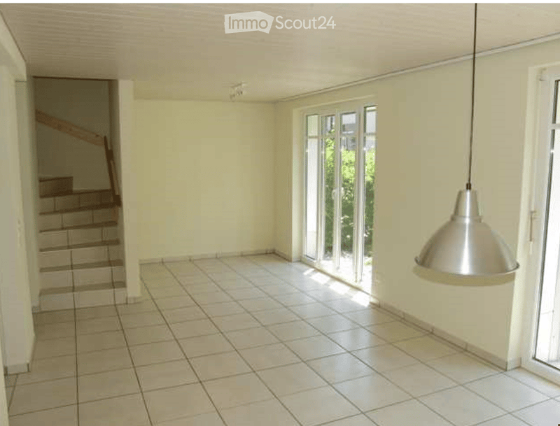 Empty room with tiled floor, white walls, large window, and staircase leading upwards.