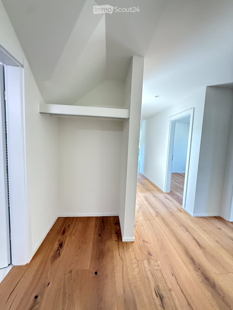 Empty room with wooden flooring and white walls, featuring a built-in closet with shelves and a doorway leading to another room.