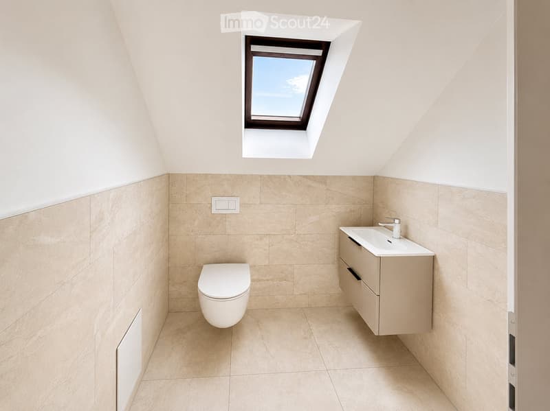 Modern bathroom with beige tiles, a toilet, a sink with a cabinet, and a skylight window.
