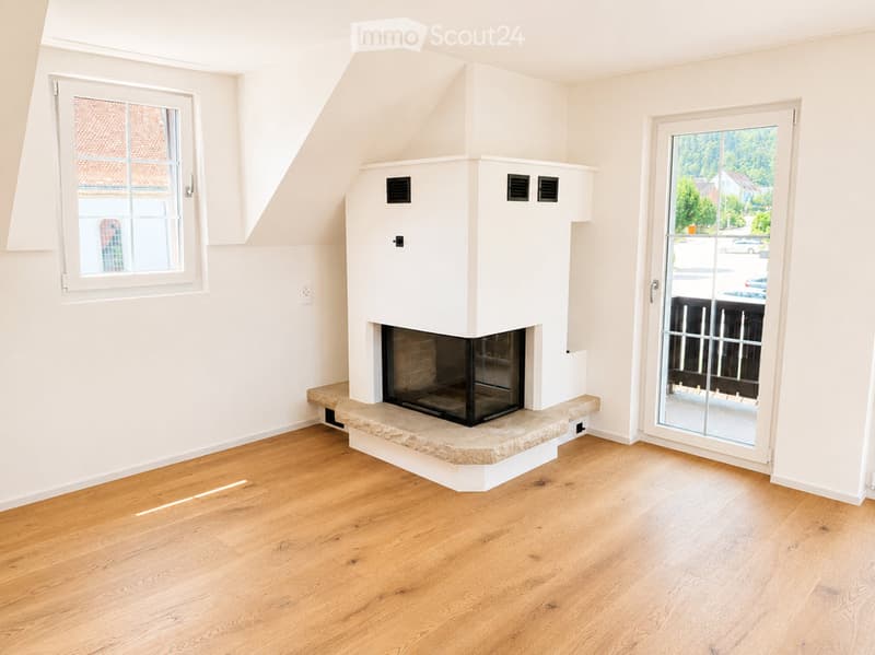Empty room with wooden flooring, white walls, fireplace, large window, and sliding glass door leading to a balcony.