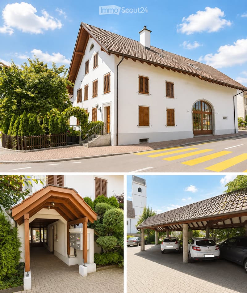 Two-story white building with brown shutters and tiled roof, featuring a covered entrance and parking area with multiple cars.