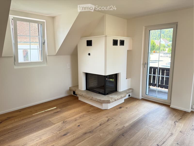 An unfurnished room with wooden flooring, a fireplace, and large windows, including a sliding glass door leading outside.