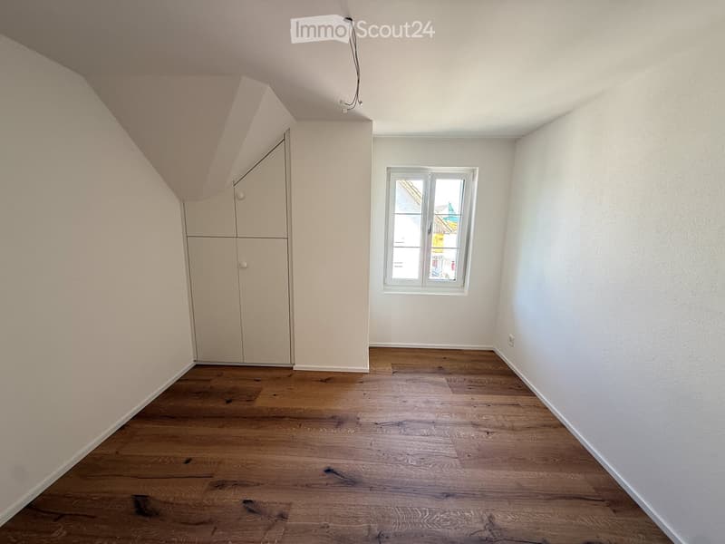 Empty room with wooden flooring, white walls, and a built-in closet. A single window provides natural light.