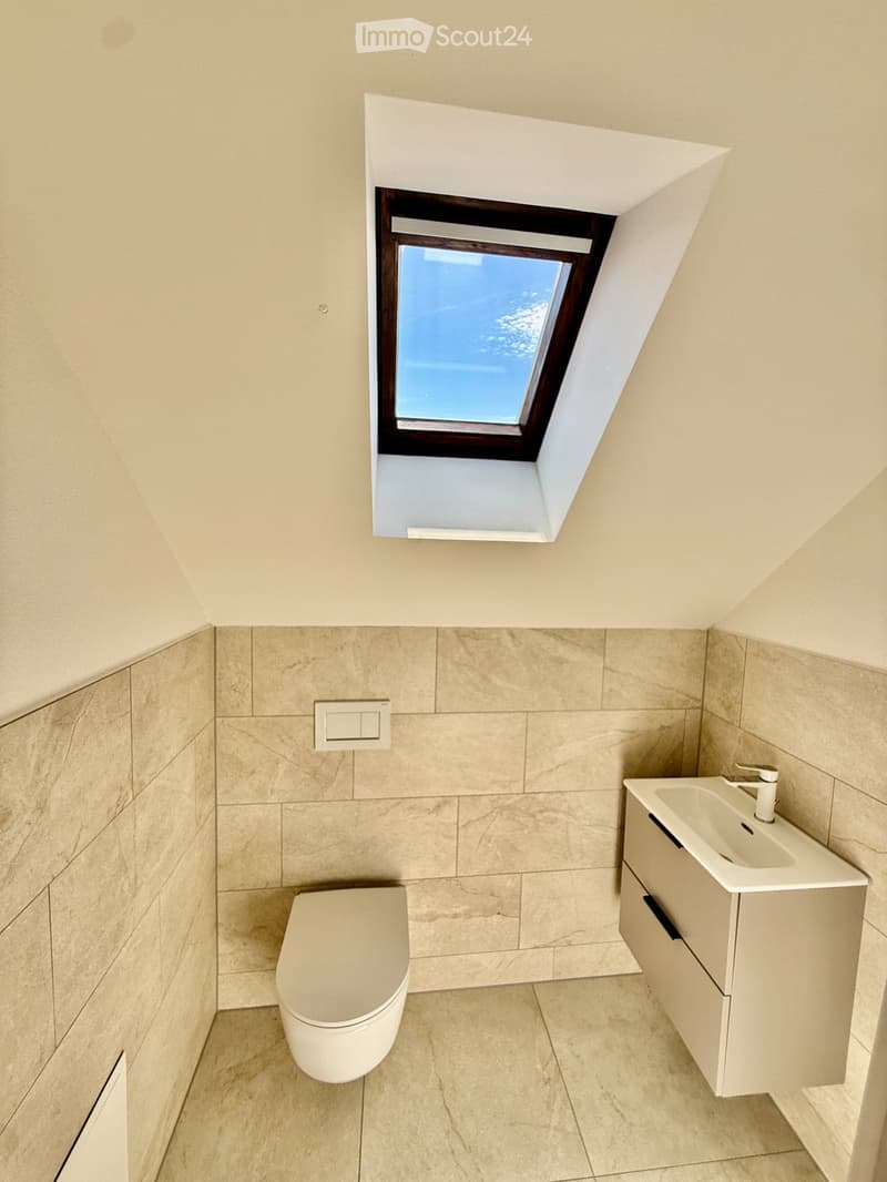 Modern bathroom with beige tiles, a toilet, a sink with a cabinet, and a skylight window.