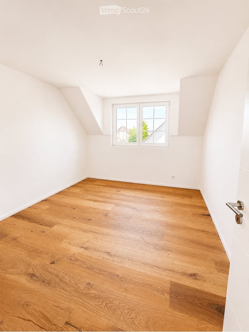 Empty attic room with wooden flooring, white walls, and a single window letting in natural light.