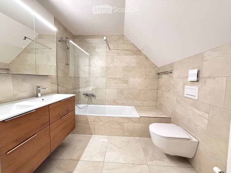 Modern bathroom with beige tiles, wooden vanity, sink, bathtub, toilet, and a large mirror.