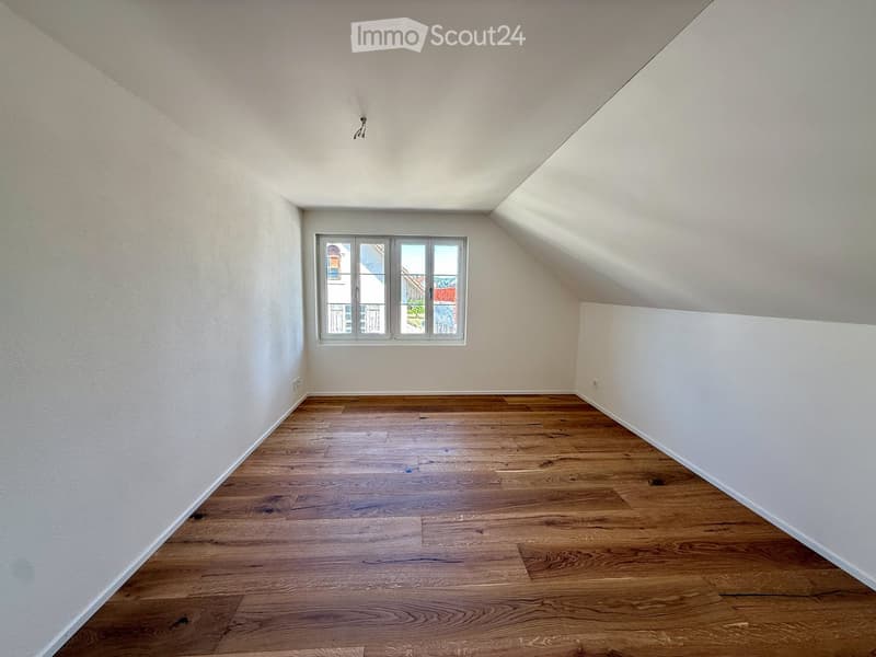 Empty room with wooden flooring and white walls, featuring a single window with multiple panes and a visible electrical outlet on the wall.
