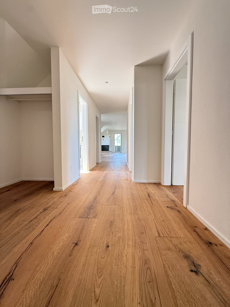 Empty hallway with wooden flooring and white walls, featuring several open doors leading to other rooms.