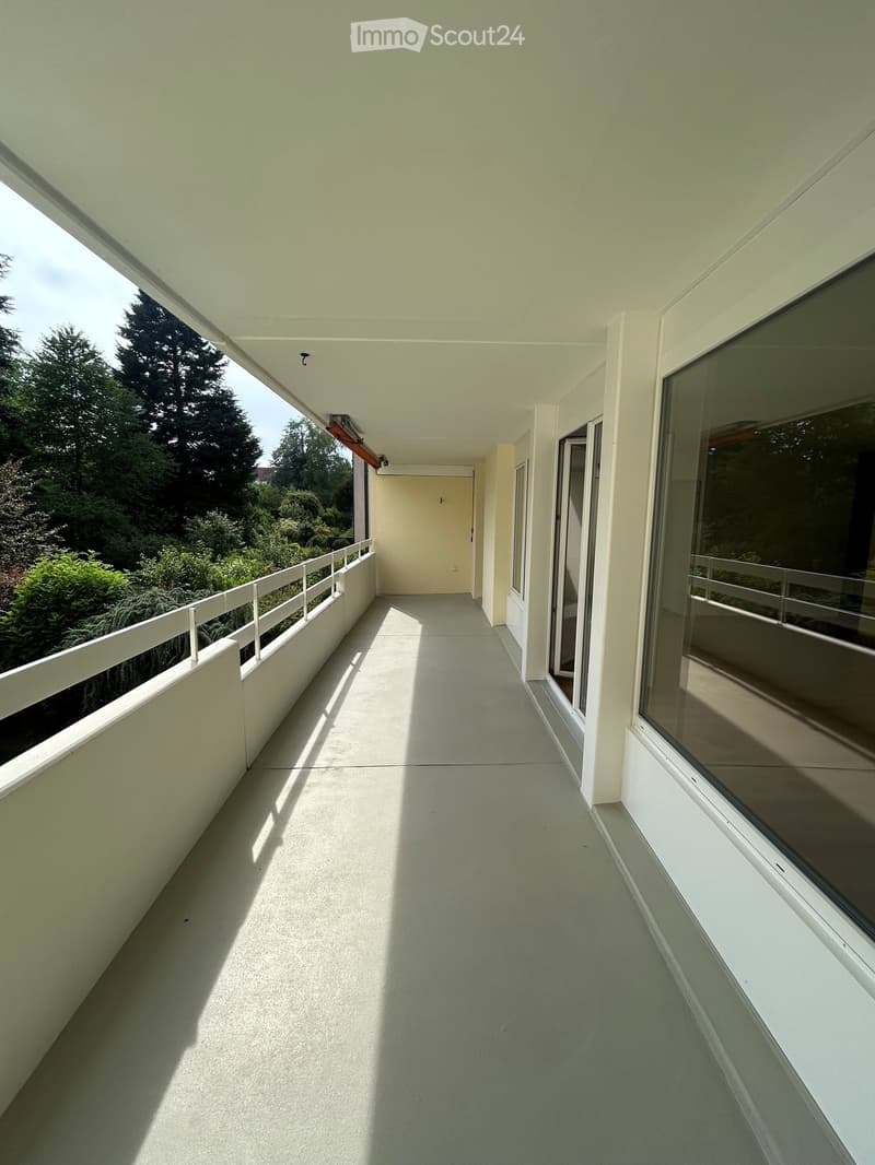 Balcony with white railings, large windows, and a view of greenery outside.