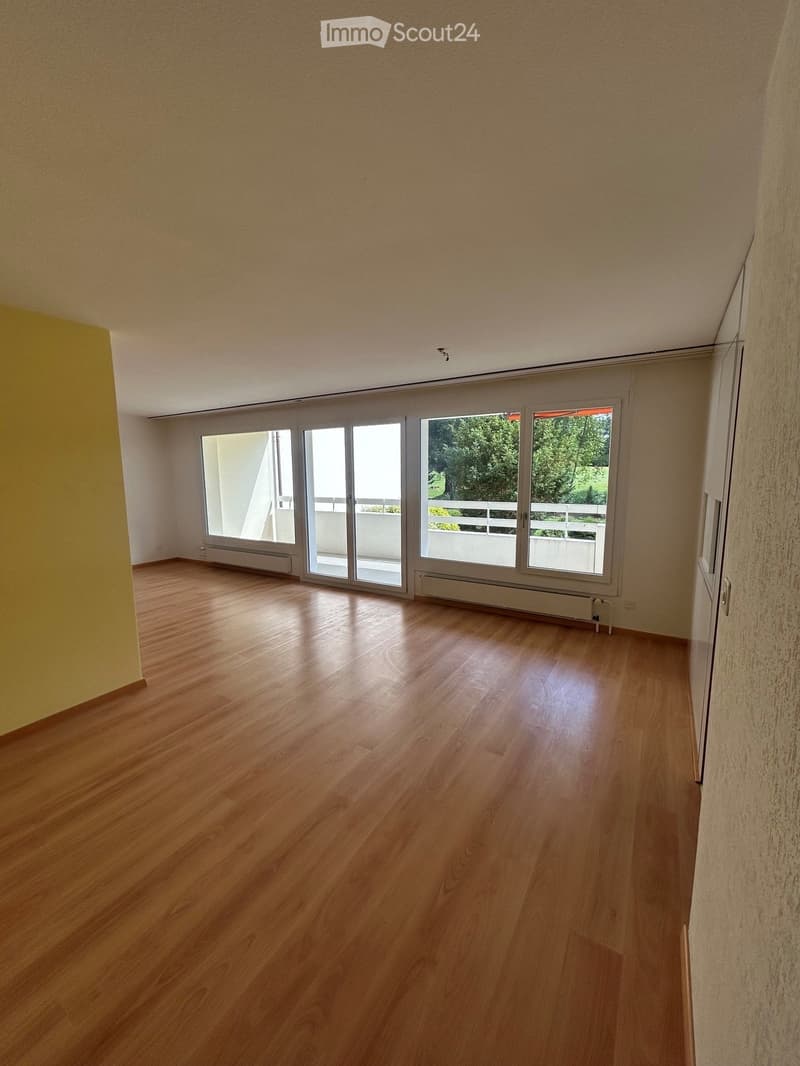 Empty room with wooden flooring, large sliding glass doors leading to a balcony, and light-colored walls.