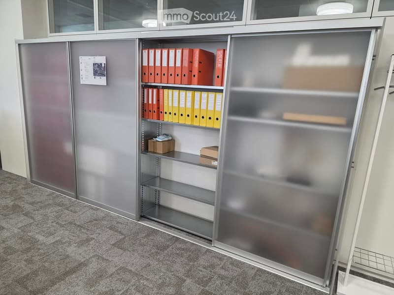 Metal cabinet with glass doors and shelves filled with red and yellow folders, small boxes, and a notepad on the floor.