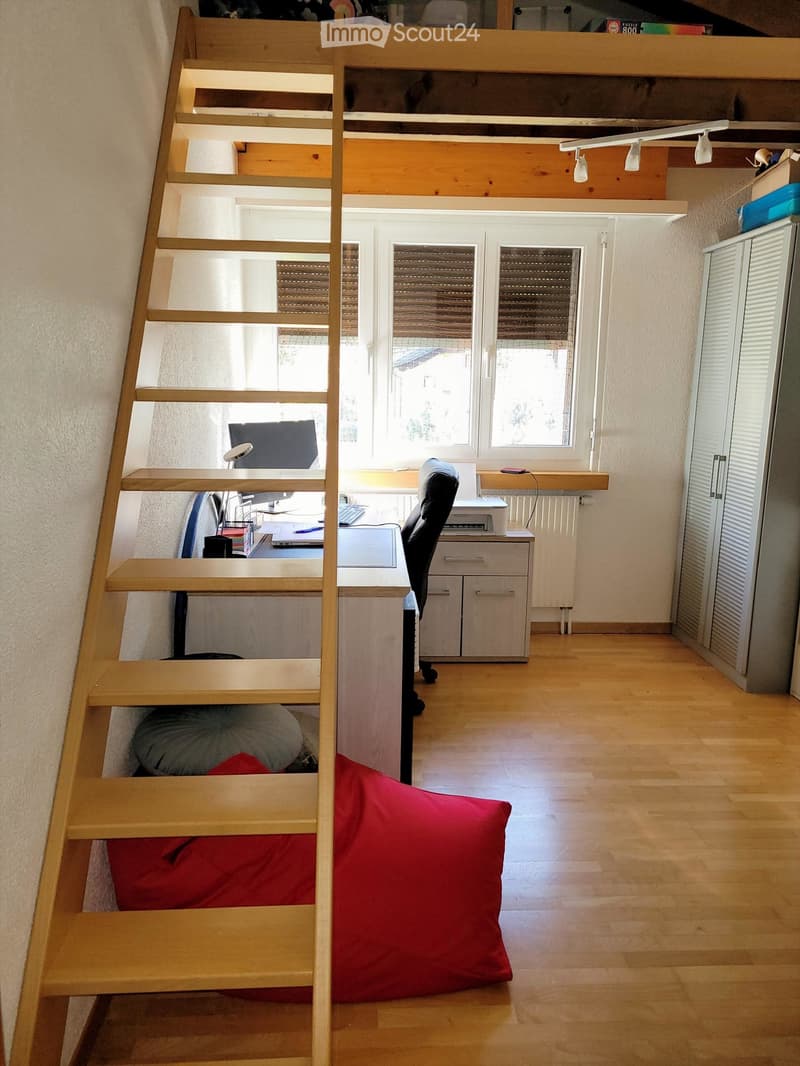 A multi-functional room with a wooden staircase leading to a loft area, a desk with a laptop and printer, a chair, a padded seat, and a cabinet.