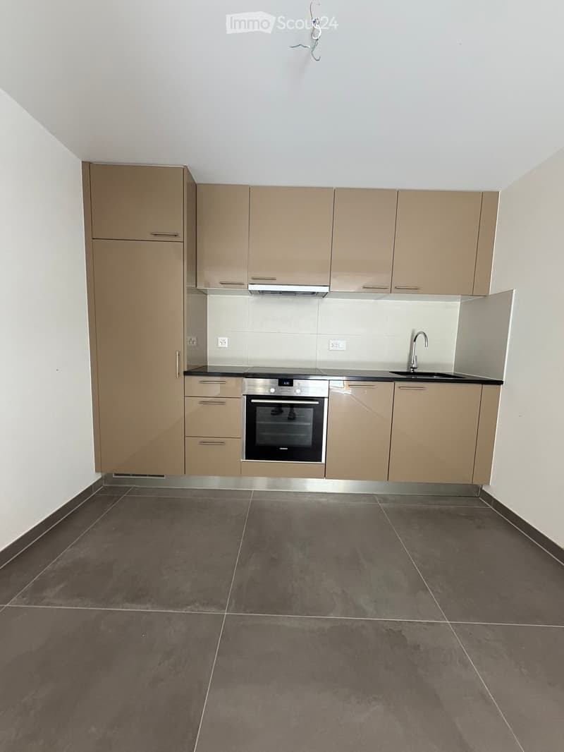 Modern kitchen with light brown cabinets, stainless steel oven, sink, and faucet, featuring dark tiled flooring and white walls.