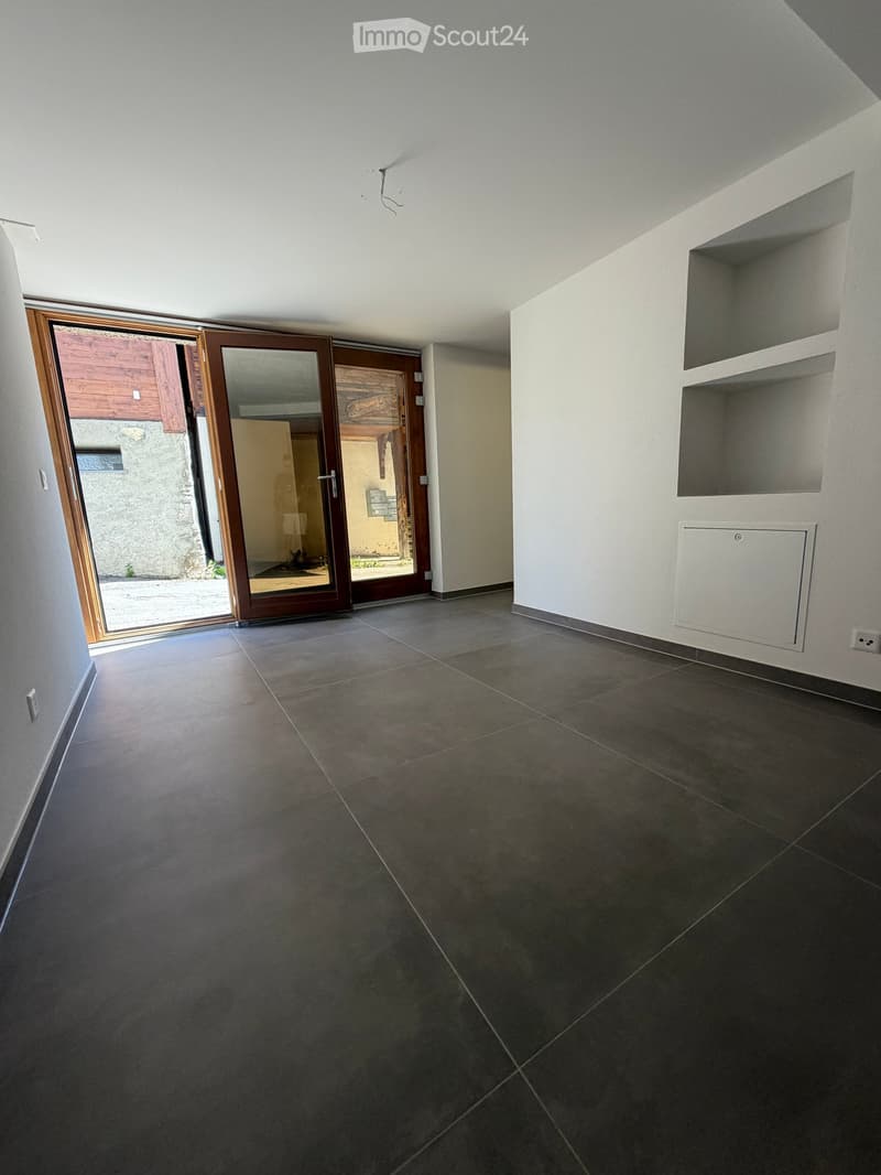 Empty room with dark tiled floor, white walls, built-in shelving, and large sliding glass door leading outside.